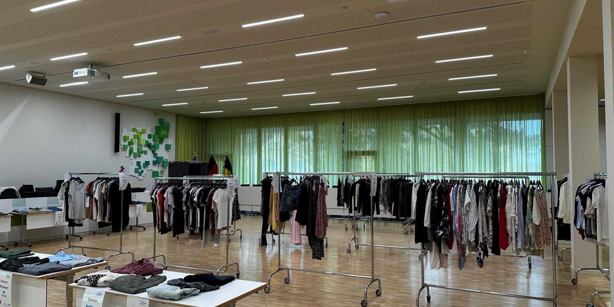 Mehrere voll behängte Kleiderständer stehen im Hohenstaufensaal des Landratsamtes. Davor und daneben stehen Tische, auf denen Kleidung ausliegt.