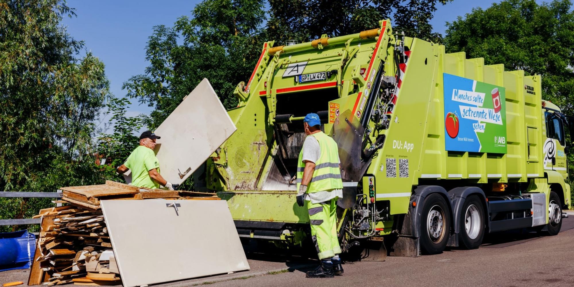 Zwei Müllwerker laden Holzteile in das Sperrmüllfahrzeug