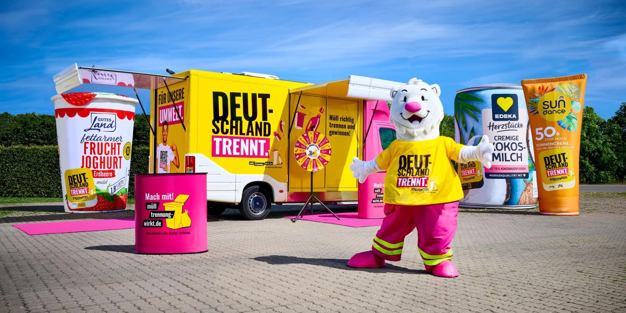 Der Trennbär steht vor dem Show-Truck mit der Aufschrift "Deutschland trennt". Drumherum stehen die XXL-Verpackungen und das Glücksrad.