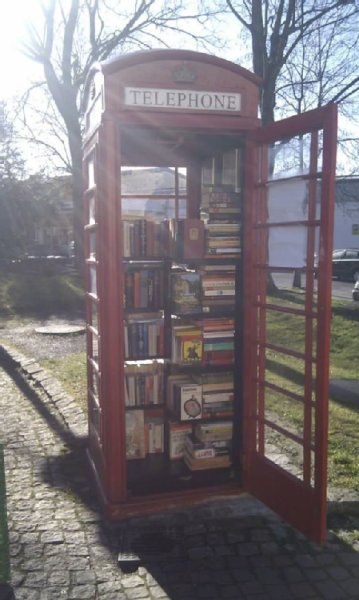 Rote Telefonzelle mit offen stehender Tür und der Aufschrift "Telephone", darin zahlreiche Bücher .