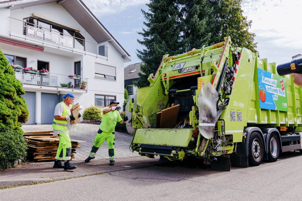 Zwei Müllwerker laden Holzteile in das Sperrmüllfahrzeug