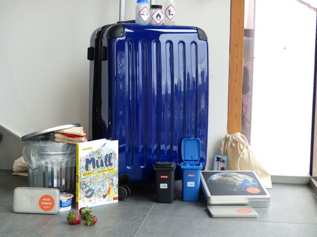 Koffer, davor Buch, Mini-Mülltonnen